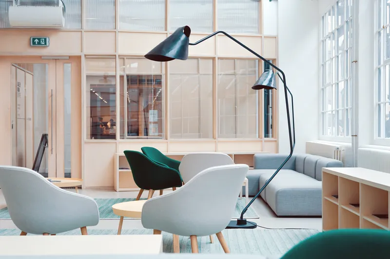 Bright modern lounge with gray and green armchairs, a gray sofa and a black arc floor lamp by tall windows
