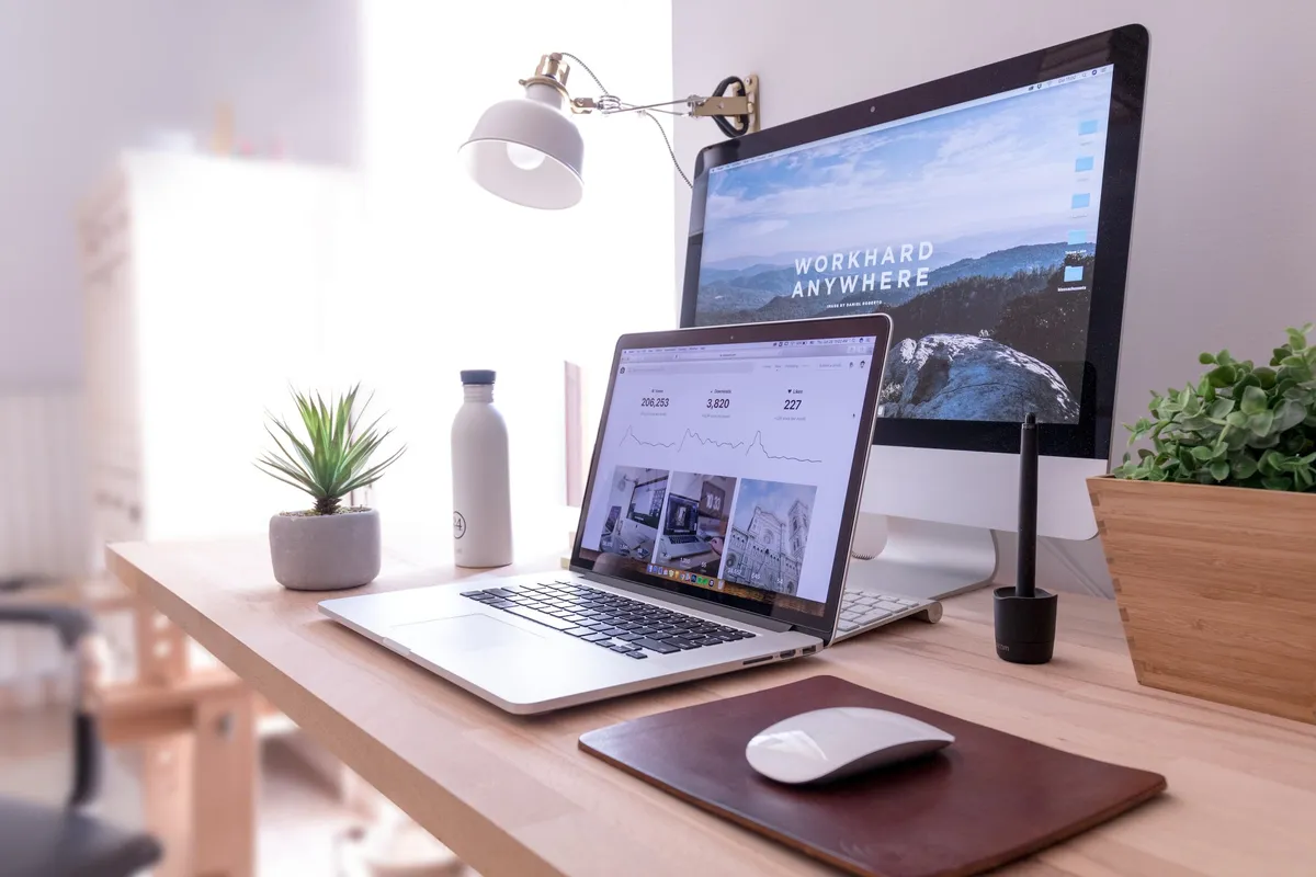 Tidy desk with a laptop showing an analytics dashboard beside a large monitor, plant and water bottle