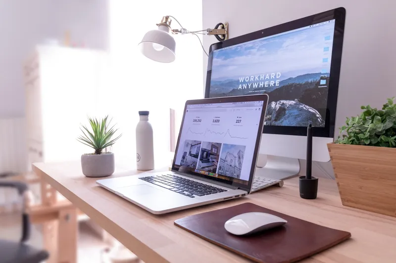 Tidy desk with a laptop showing an analytics dashboard beside a large monitor, plant and water bottle