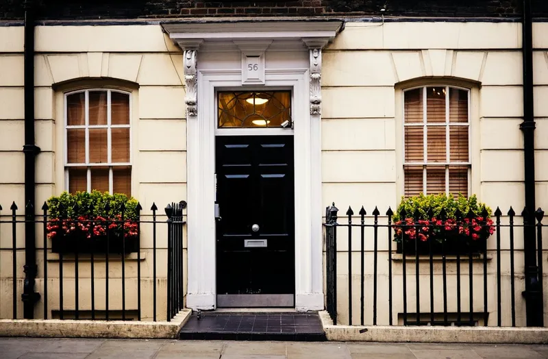 Glossy black front door numbered 56 on a cream townhouse with iron railings and red flower boxes