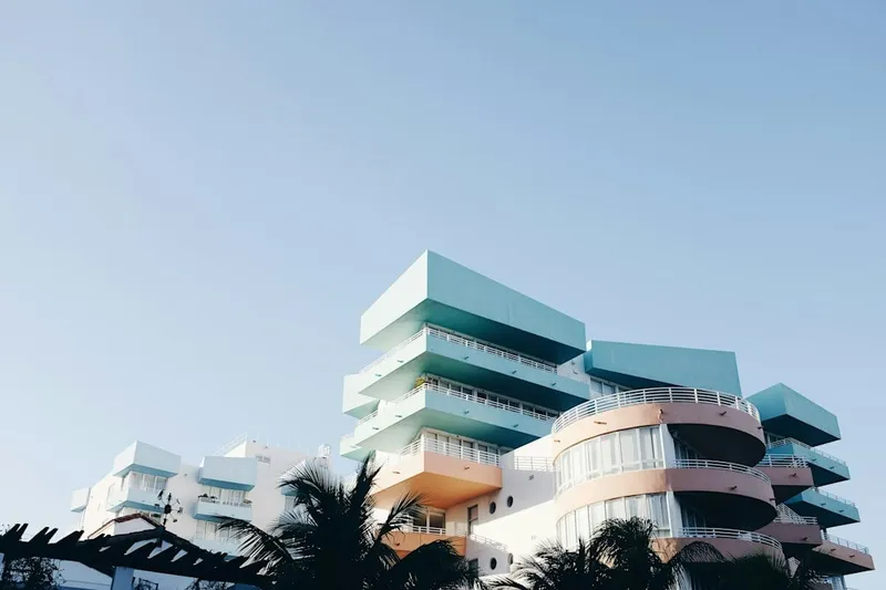 Pastel blue and peach Art Deco apartment building with curved balconies and palm trees under a clear sky