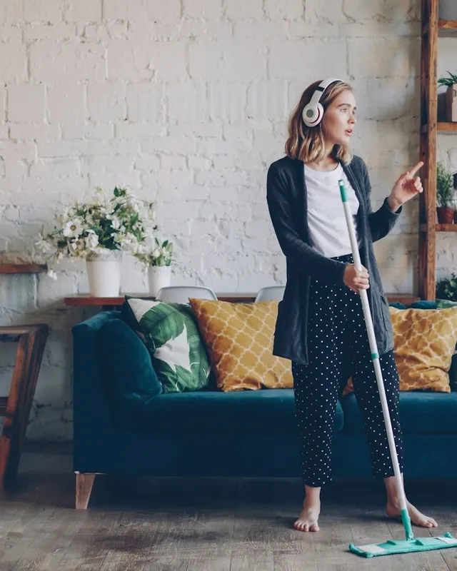 Femme avec un casque audio passant la serpillière dans un salon lumineux