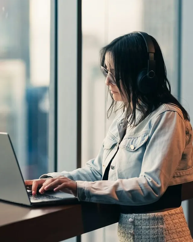 Femme avec un casque audio travaillant sur un ordinateur portable près d'une fenêtre