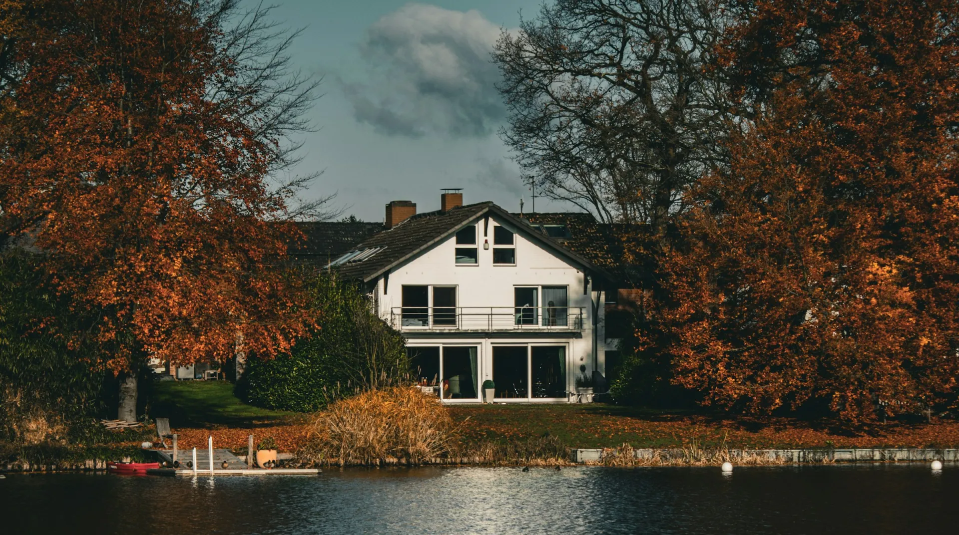 A lakefront house framed by autumn trees